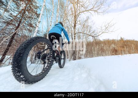 Fat bike biking girl riding on snow trail path in winter. Outdoor sport in nature landscape Stock Photo