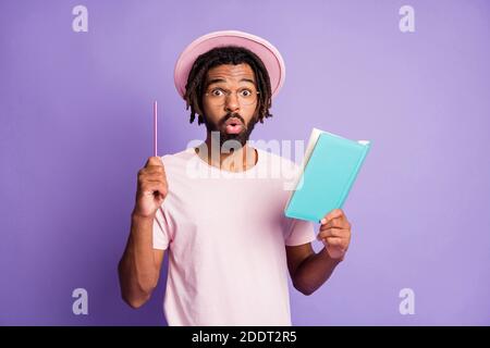 Photo of young afro amazed surprised handsome man male guy point pen in copyspace hold blue diary isolated on violet color background Stock Photo