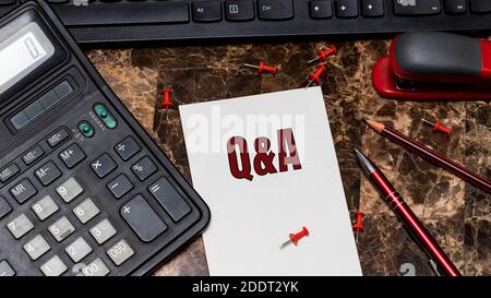 Q and A word is written on a piece of paper that is on the desktop next to the calculator and office supplies. FAQ, frequency asked questions, Informa Stock Photo