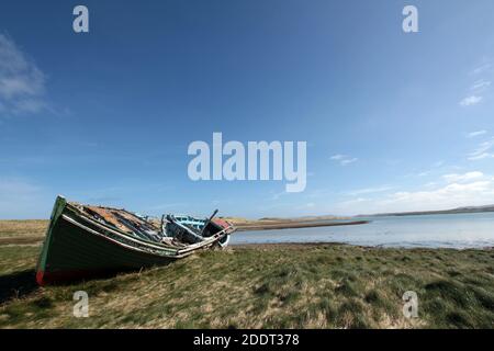 The decaying wreck of an old fishing boat lies on the grass near the shoreline Stock Photo