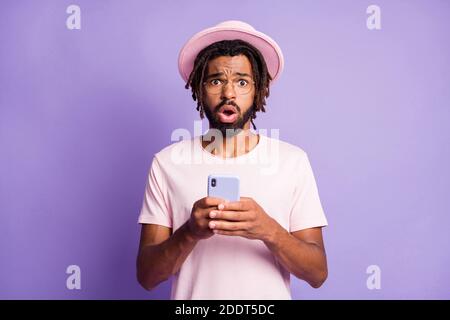 Photo portrait of confused guy holding phone in two hands isolated on vivid purple colored background Stock Photo
