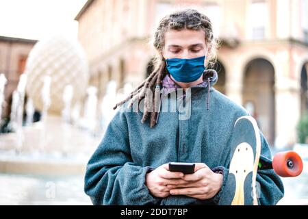 Unhappy guy with protective mask using tracking app on mobile smartphone - Young worried millenial sharing content on social media Stock Photo