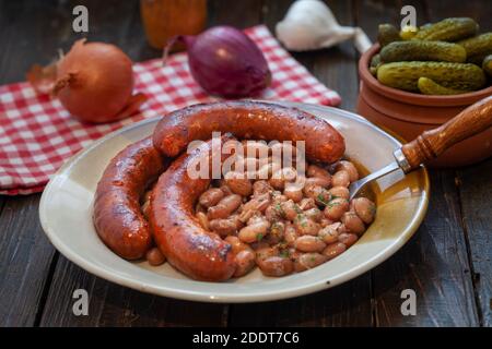 Baked beans with grilled sausage, traditional Balkan homemade meal.  Plate with spicy pork sausages and beans. Stock Photo