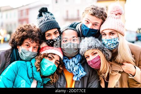 Multiracial friends taking selfie wearing face mask and winter clothes - New normal lifestyle concept with young people having fun together outside Stock Photo