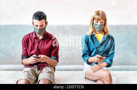 Bored addicted couple with protective masks using tracking app with mobile smartphones - Young millenial man and woman sharing content on social media Stock Photo