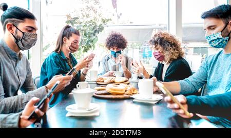 Millenial people using mobile smart phones at coffee bar - New normal lifestyle concept with friends checking contact tracing app during pandemic Stock Photo