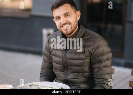 Handsome man sitting outdoors in cafe on terrace and smiled to camera Stock Photo