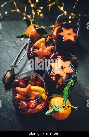 Table stilllife with Mulled wine with spices, fruits, cinnamon served in thin glass mugs with unfocused xmas tree lights on background. Christmas and Stock Photo