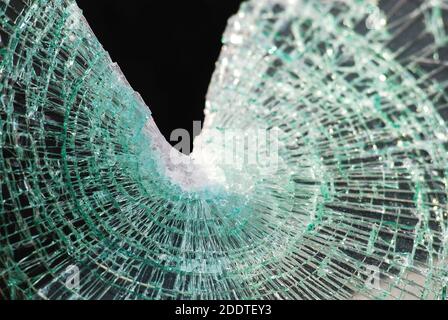 Shattered laminated glass from a windshield display classic spider web cracking after impact with a triangular gap on the top. Black background. Stock Photo
