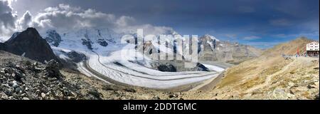 Diavolezza mountain cable car station panorama of the surrounding mountain range and glacier on a sunny blue sky autumn day, clouds closing from far. Stock Photo