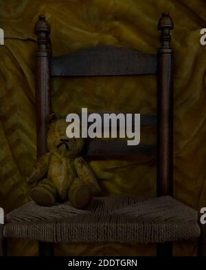 Yellow teddy sitting on wooden chair with material background Stock Photo