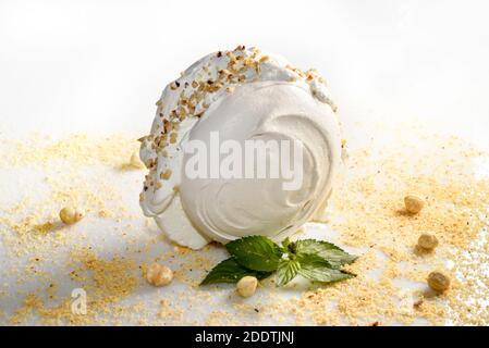 whipped cream-filled meringue with chopped hazelnuts and mint leaves on a white background Stock Photo