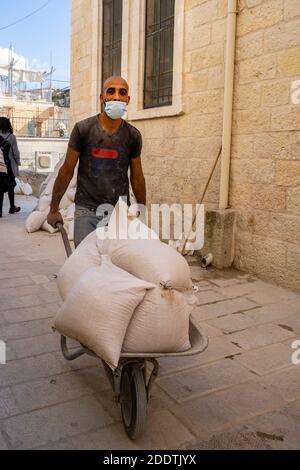 Jerusalem, Israel - November 21st, 2020: A construction worker, wearing a protective mask, pushing a wheelbarrow full of building materials in old Jer Stock Photo