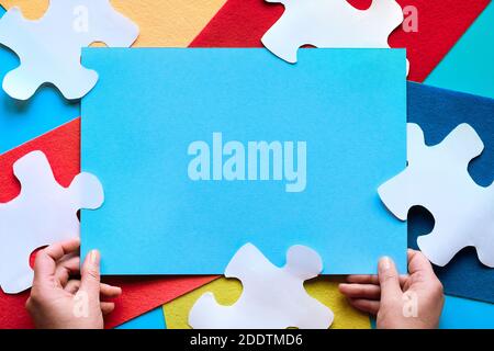 Hands hold blue paper page with copy-space. Frame made of layered colorful felt and puzzle pieces. Stock Photo