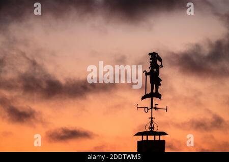 Wind vane in the shape of a cane man, silhouetted against a sunset sky. Stock Photo