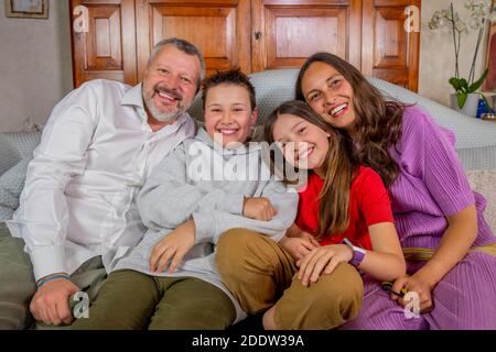 Happy family portrait - Father, mother, son and daughter laughing together sitting on sofa Stock Photo