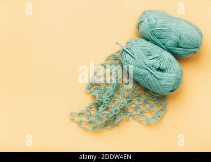 Clews of green threads and knitted plaid on light yellow background, copy space Stock Photo