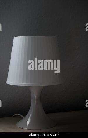 Vertical image of a white bedside lamp on a side-lit nightstand. Dark photography Stock Photo