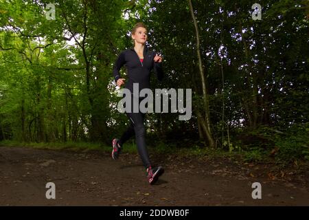 Young woman trail running in the woods in the UK. Stock Photo