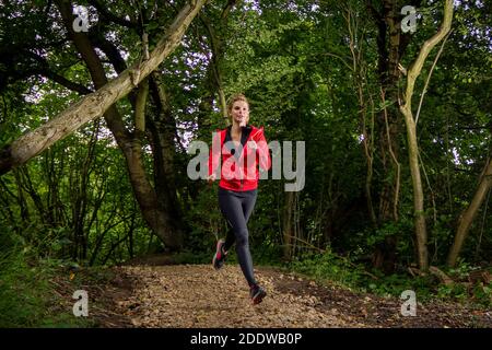 Young woman trail running in the woods in the UK. Stock Photo