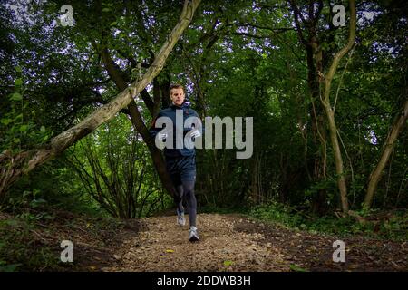 Young man trail running on a gravel path in the woods, UK. Stock Photo
