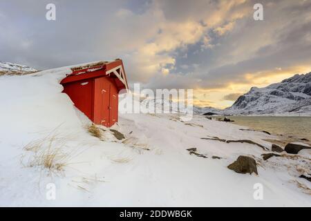 Lofoten Islands in Norway and their beautiful winter scenery at sunset. Idyllic landscape with red house on snow covered beach. Tourist attraction in Stock Photo