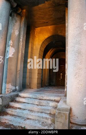 Entrance door of a decayed building with classic columns, stairs and arcade Stock Photo