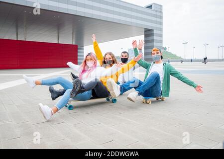Group of teenagers covered by  face masks fooling about at skate park - Multiracial students on skateboard at college campus - Concepts lifestyle Stock Photo