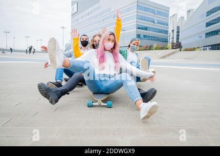 Group of teenagers covered by  face masks fooling about at skate park - Multiracial students sitting on skateboard at college campus - Concepts lifest Stock Photo