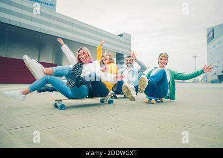 Group of teenagers fooling about at skate park - Happy young friends sitting on skateboard - Group of cheerful friends having fun, concepts about teen Stock Photo