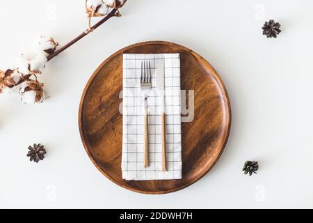 Feminine wedding, birthday desktop mock-up scene. Wooden dish, cutlery with checkered napkin, cotton flowers. White table background. Flat lay, top Stock Photo