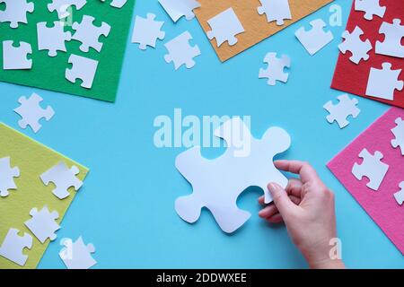Hand holding large puzzle element. Jigsaw puzzle pieces, multicolor felt sheets on blue background. Stock Photo