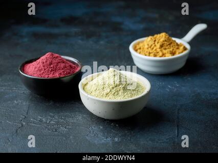 three bowls of dried plant powder on deep blue painted background Stock Photo