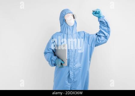 male doctor in a protective medical suit to protect against coronavirus, in a mask, glasses and gloves, with a laptop shows the gesture of victory, on Stock Photo