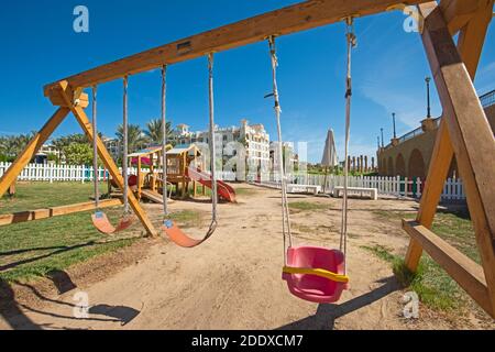 Swings frame structure in children's playground area with slide at tropical resort hotel Stock Photo