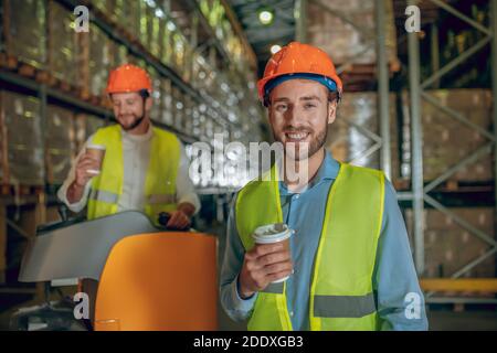 Warehouse workers in orange helmets having coffee break Stock Photo