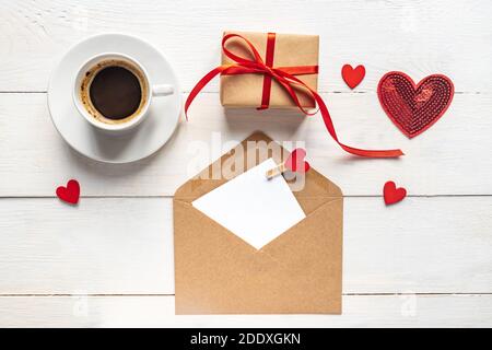 Valentines day mockup. Coffee, gift box and paper card with craft envelope on white wooden table top view. Flat lay style Stock Photo