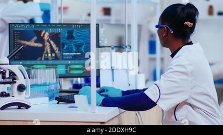 African woman biochemist researcher checking manifestations of vaccine working in modern equipped laboratory. Multiethnic doctors examining virus evolution using high tech researching diagnosis Stock Photo