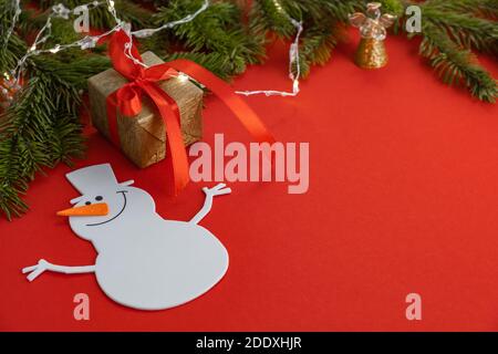 Creative Christmas card.Funny snowman on red background with gift,garland and sprigs of spruce.The concept of meeting Christmas and New Year.Copyspace Stock Photo