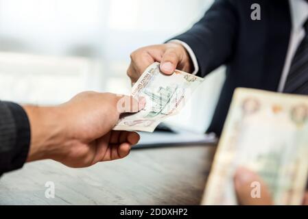 Businessman giving money, United Arab Emirates dirham currency, to his partner Stock Photo