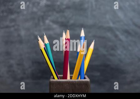 Assorted colorful sharp pencils standing in holder on blurred chalkboard background Stock Photo