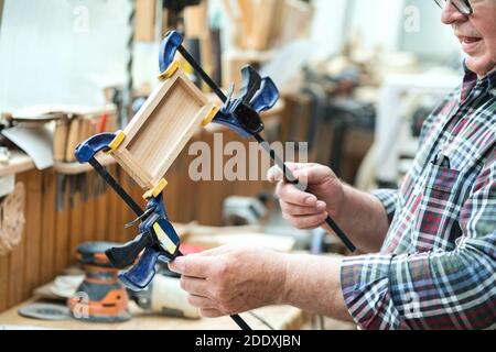 Senior carpenter glueing wooden craft surface and joining with clamps. Woodwork carpenter with equipment and tools at workshop. Handmade diy furniture Stock Photo