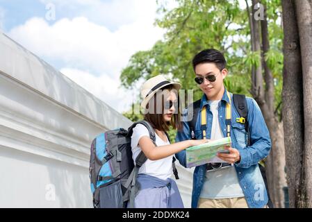 Asian couple tourist backpackers looking at the map beside temple wall while traveling on holidays in  Bangkok, Thailand