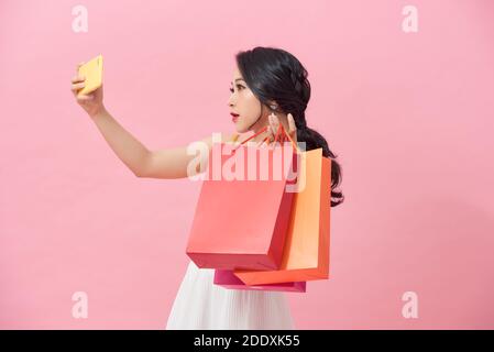 Happy pretty young woman with shopping bags makes photo self-portrait on the smartphone over colorful wall Stock Photo