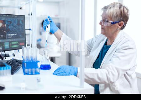 Senior chemist woman using molecular dropper during healthcare experiment. People in innovative pharmaceutical laboratory with modern medical equipment for genetics research. Stock Photo