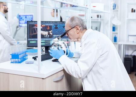 Senior scientist preparing and analyzing microscope slides with busy coworkers. Chemist researcher in sterile lab doing experiments for medical industry using modern technology. Stock Photo
