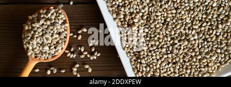 organic dried hemp food seeds in a ceramic plate and rustic wooden spoon on dark wooden background. flat lay. banner Stock Photo