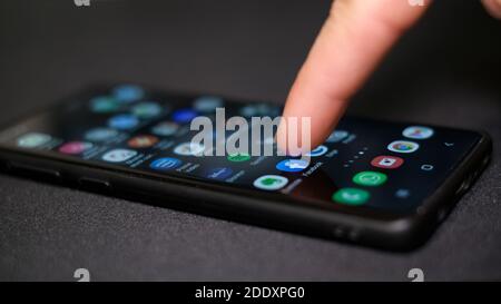 Man hand close up while tapping on Facebook app icon on a smartphone,social network tech addiction Stock Photo