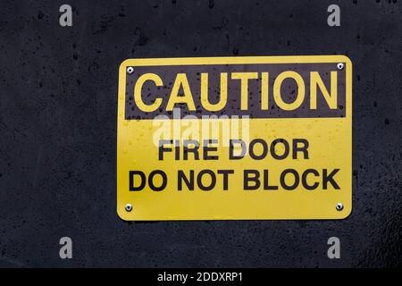 View of yellow sign Caution Fire Door Do Not Block against the black background Stock Photo