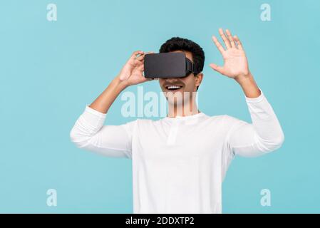 Excited Asian man enjoying watching  3D simulation video from virtual reality or VR glasses on light blue background Stock Photo